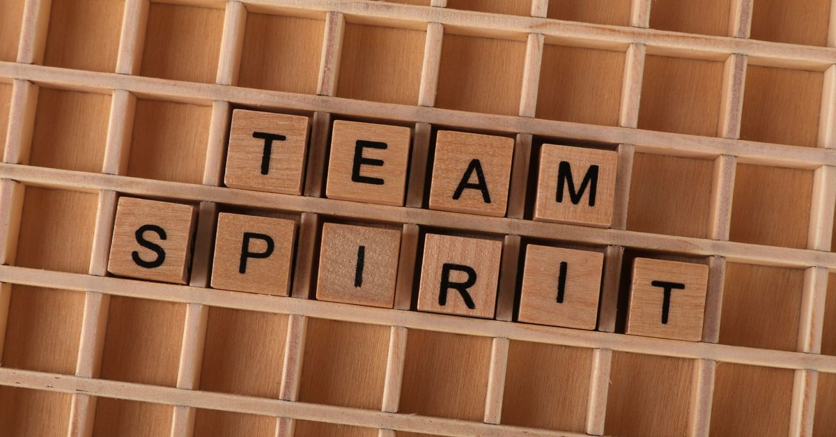 Wooden Scrabble tiles arranged to spell 'Team Spirit' on a wooden grid.